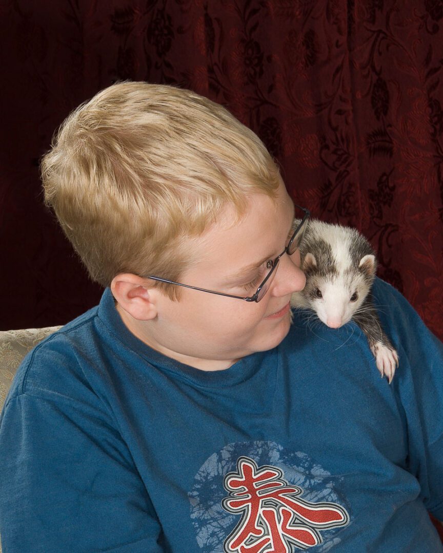 A boy with glasses and a blue shirt is holding a small hamster
