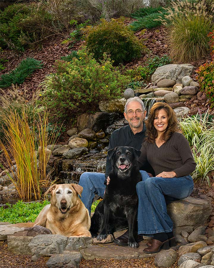 A man and woman sitting on rocks with two dogs.