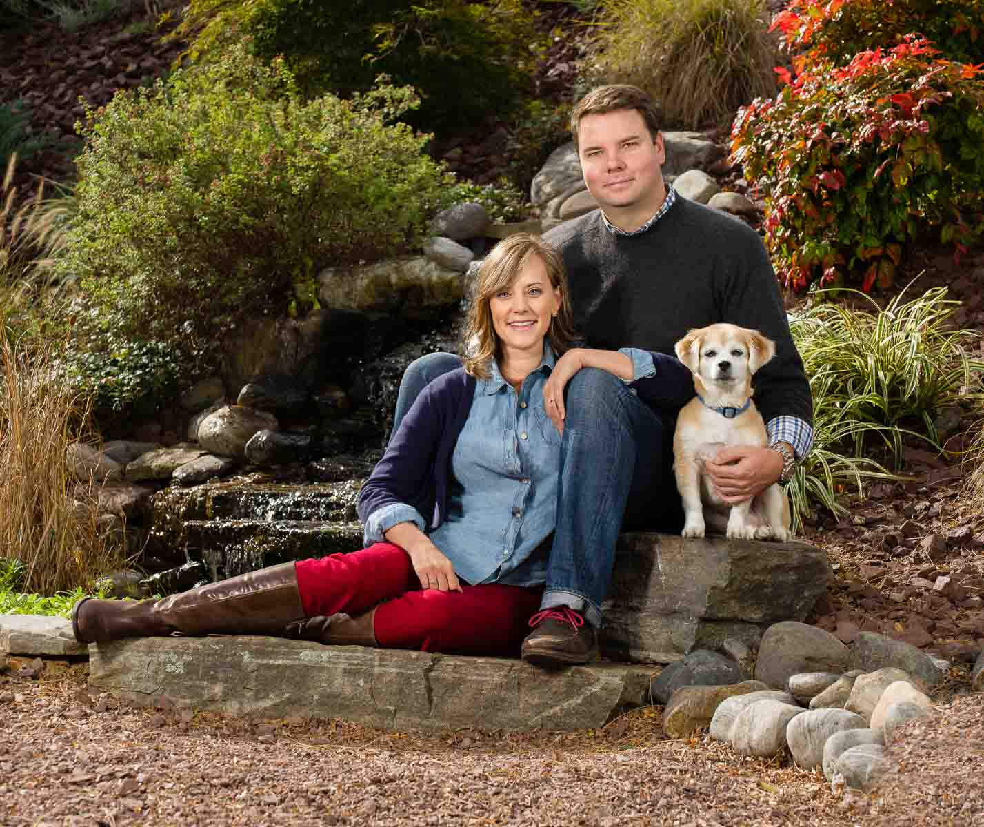 A man and woman sitting on top of rocks with their dog.