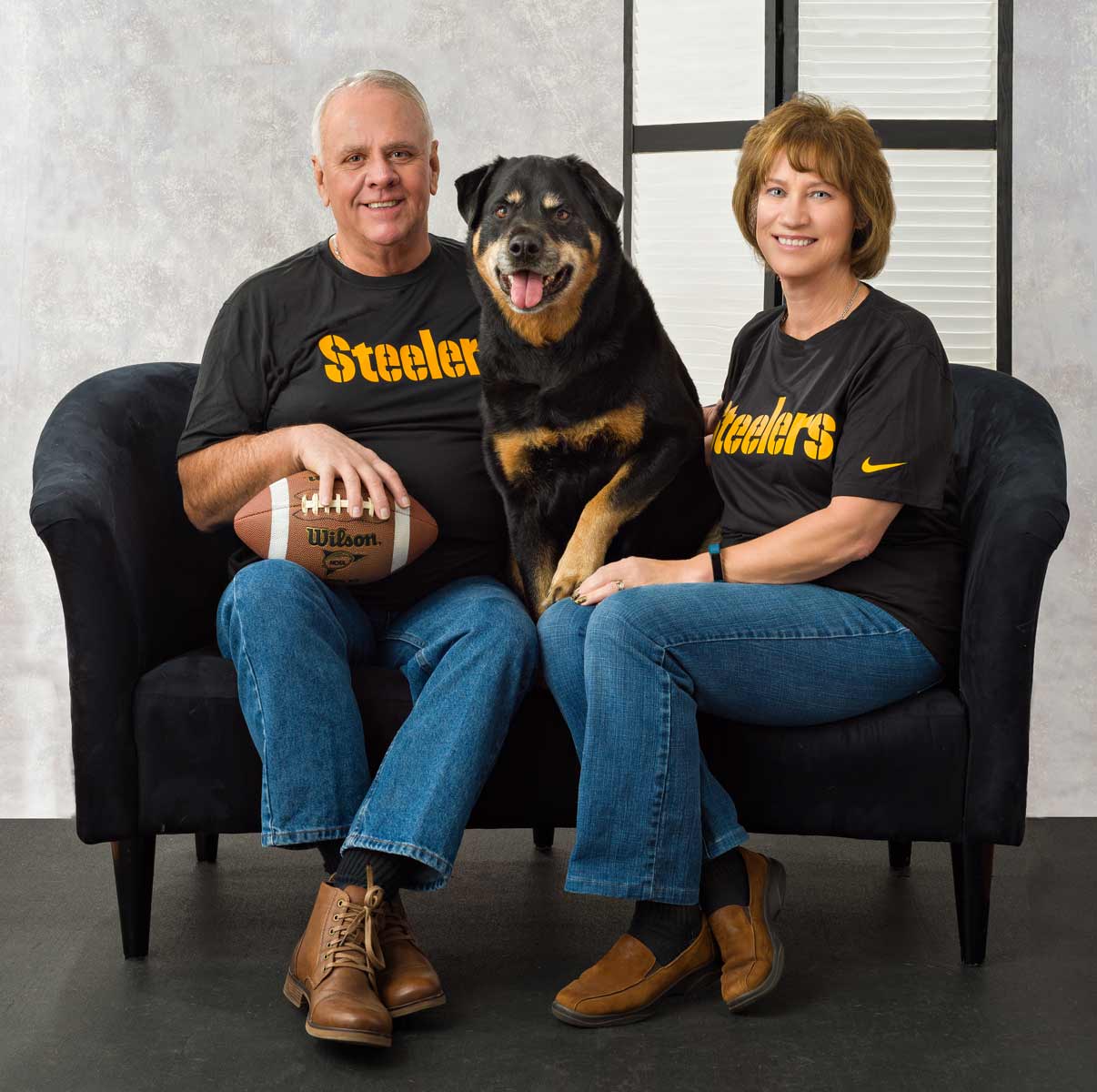 A man and woman sitting on a couch with their dog.