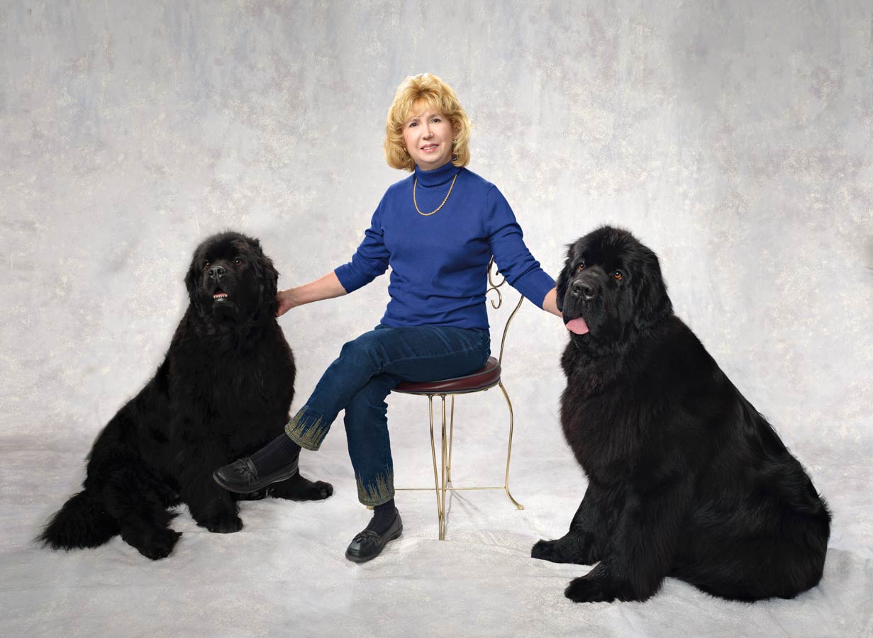 A woman sitting on a chair with two black dogs.