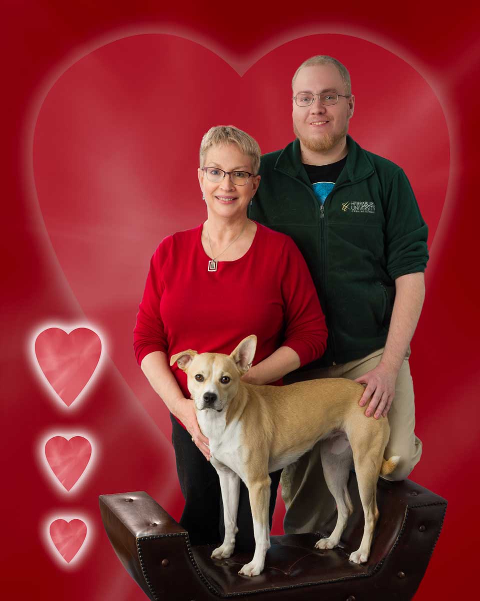 A man and woman with their dog in front of hearts.