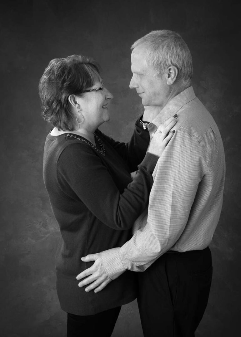 A man and woman are hugging in front of a black background.
