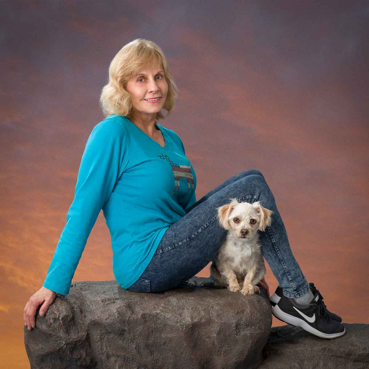 A woman sitting on top of a rock with her dog.