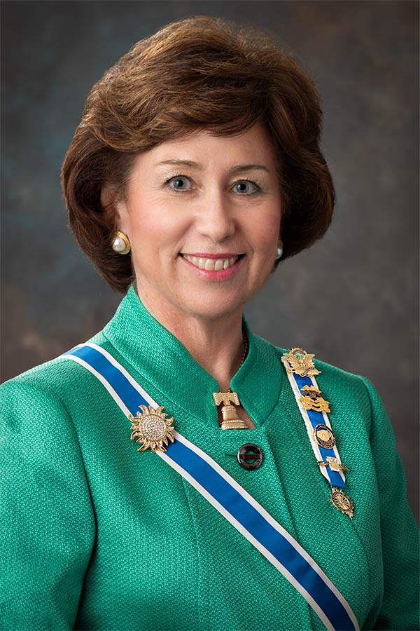 A woman in green jacket with blue and white ribbons around her neck.