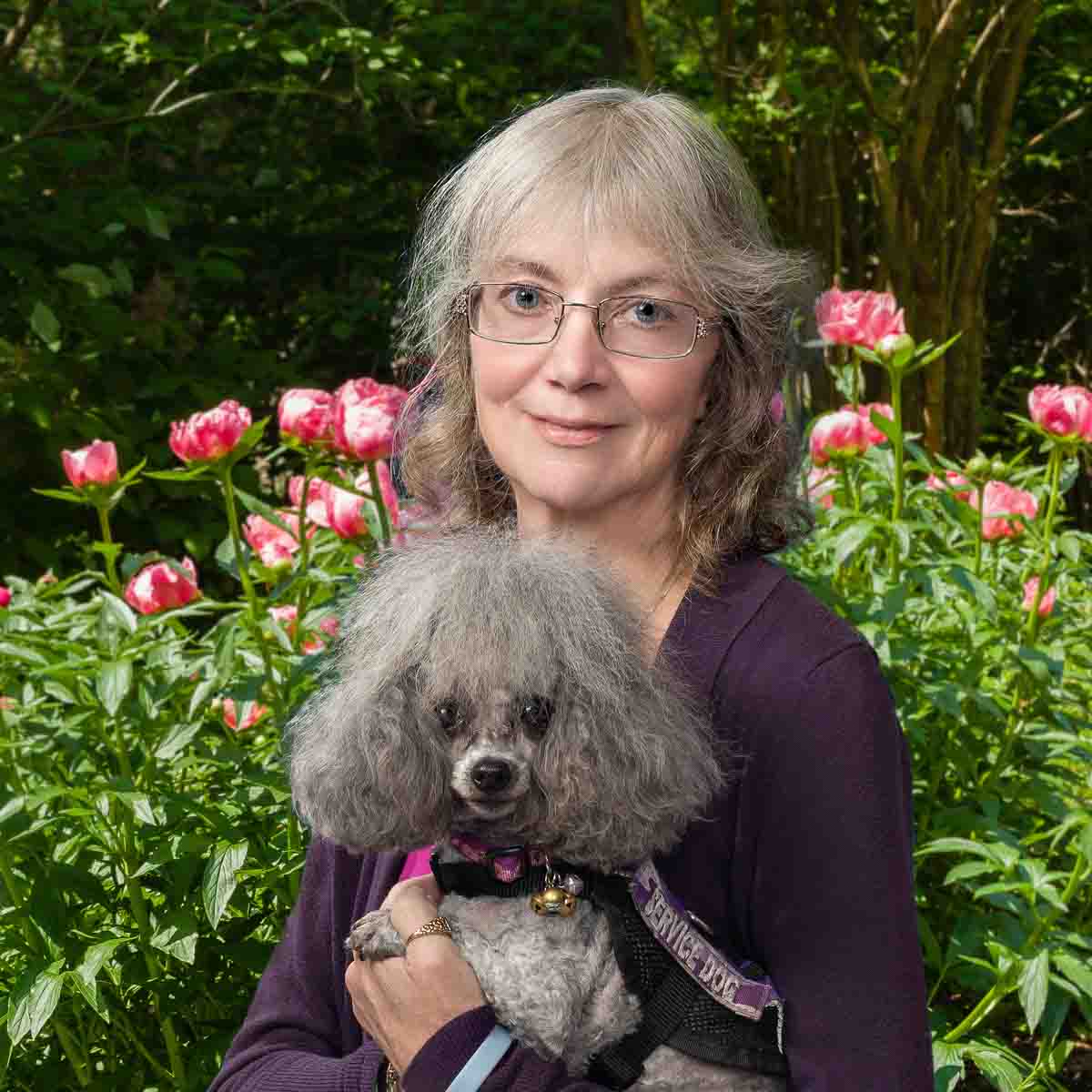 A woman holding her dog in front of some bushes