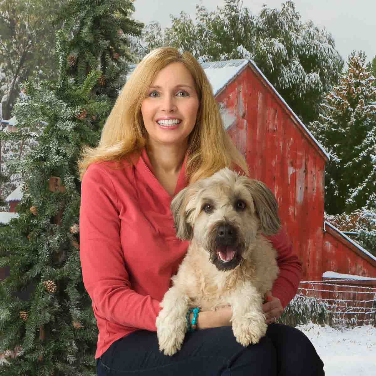 A woman holding her dog in front of a red barn.