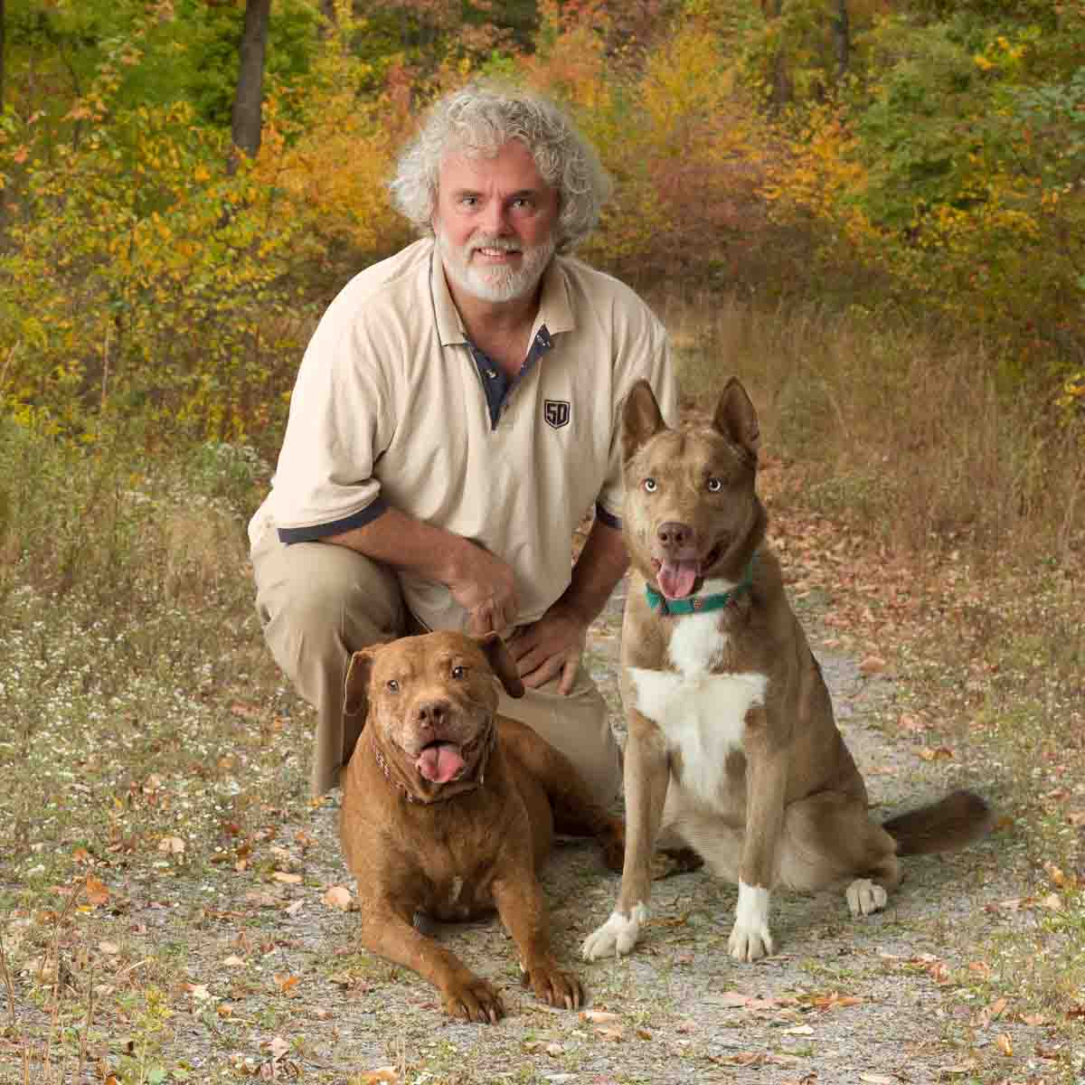 A man kneeling down next to two dogs.