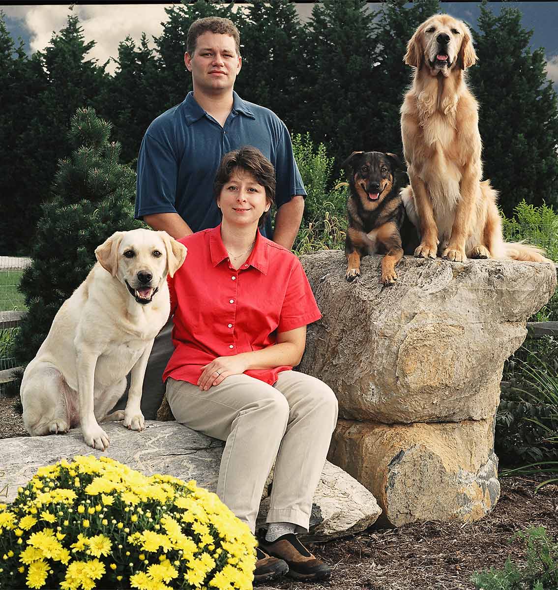 A man and woman sitting on top of a rock with two dogs.