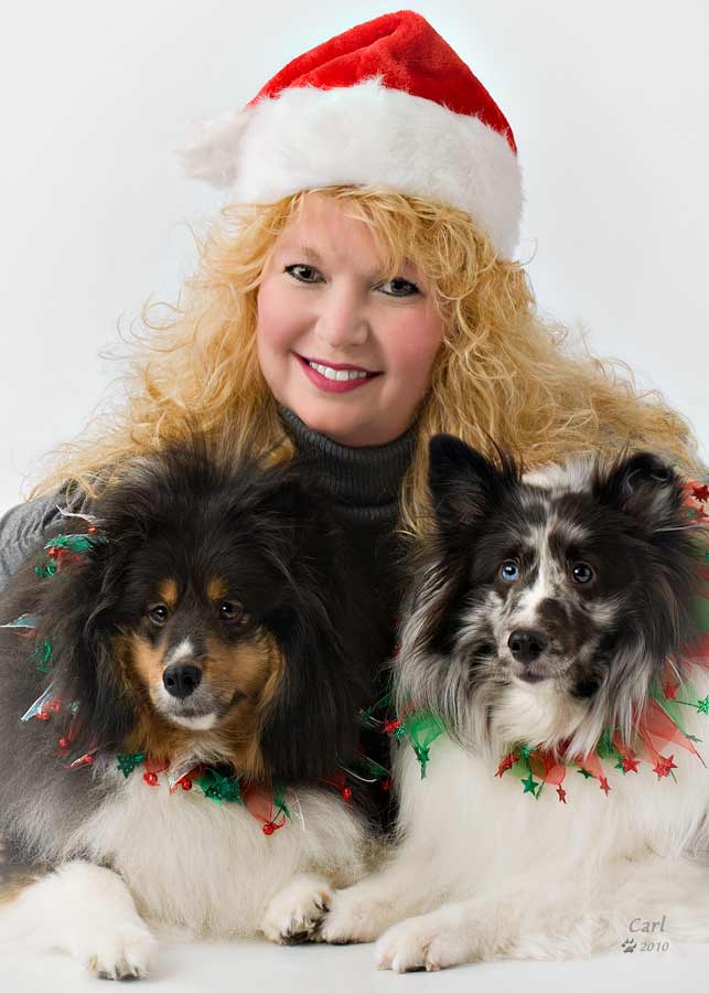 A woman wearing a santa hat and holding two dogs.