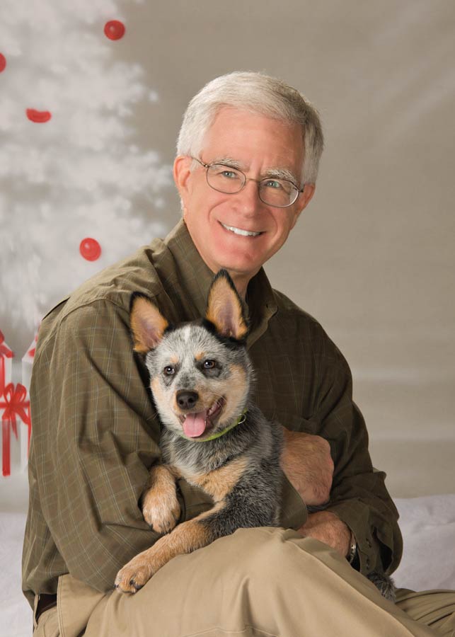A man holding his dog in front of a christmas tree.