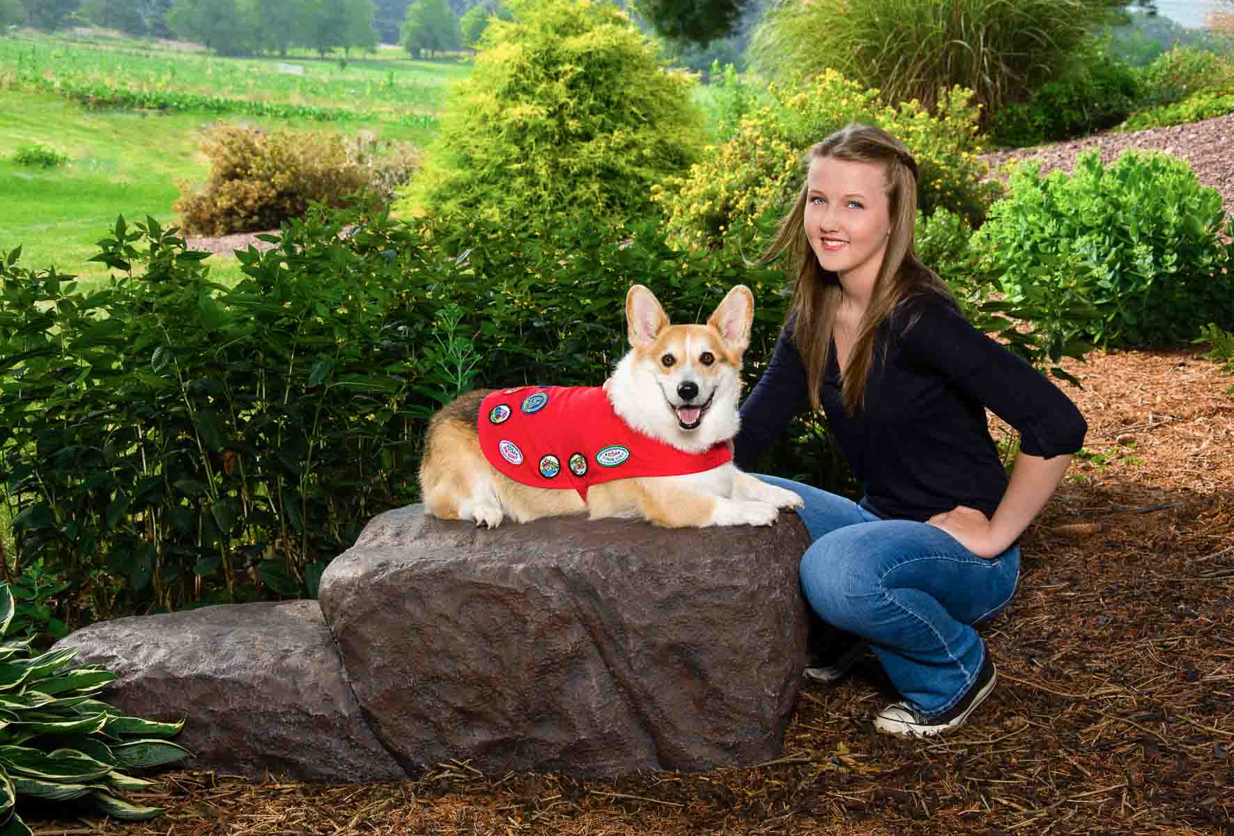 A woman and her dog sitting on top of a rock.